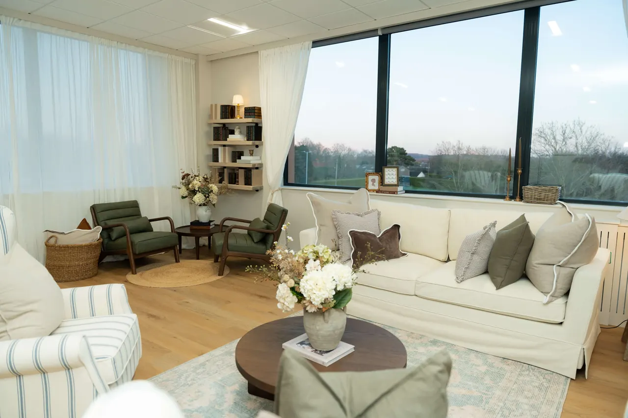 Wide view of the lounge with sofa, green chairs and parkland window