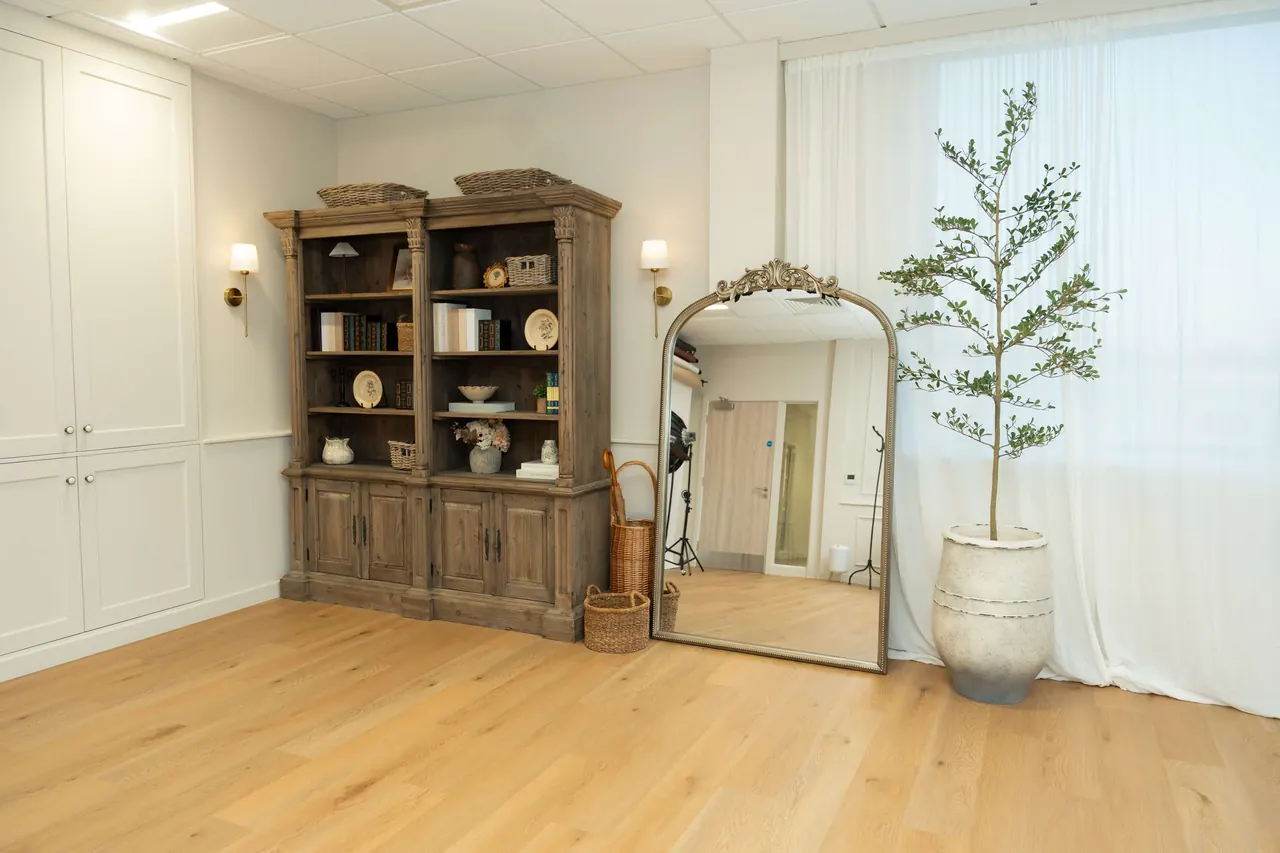 Tall arched mirror beside wooden cabinet with olive tree
