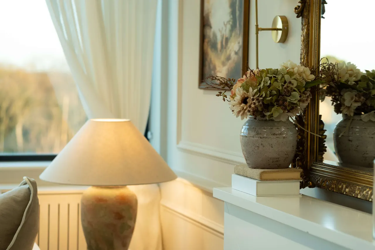 Warm window light on lamp, gilt mirror and styled flowers